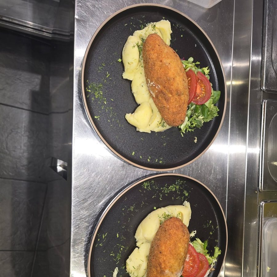 Two dark plates, each with a breaded croquette on mashed potato with tomato and herbs.