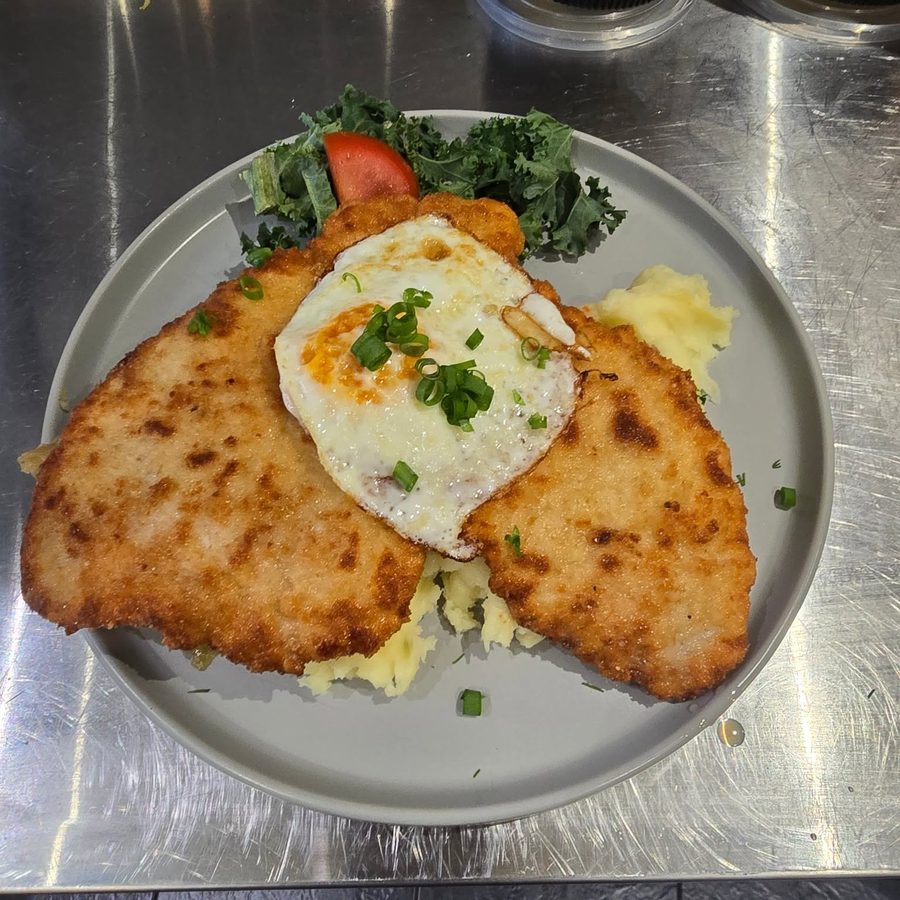 Two golden breaded pork cutlets on a plate with mashed potato, a fried egg on top and a side salad.