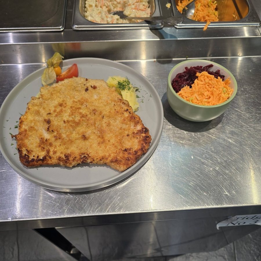 A breaded cutlet on a plate beside small bowls of grated carrot salad and beetroot.