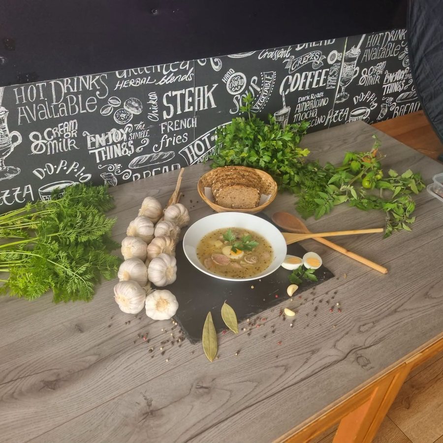 A bowl of mushroom soup on a dark board, surrounded by fresh mushrooms, herbs and bay leaves.