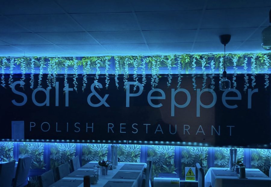The restaurant's dining room at night, tables laid with white cloths beneath a lit Salt & Pepper sign.